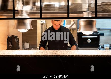 An expert chef meticulously prepares food in a modern restaurant kitchen, displaying concentration and culinary skills under bright lights Stock Photo