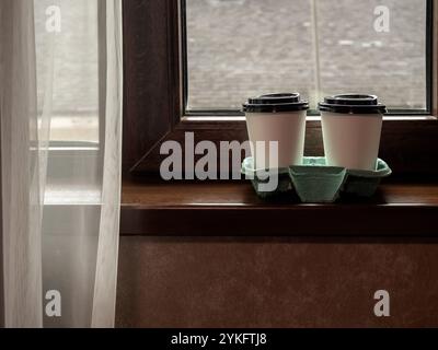Two white coffee cups in carry tray for takeaway, on the wooden window edge near in the bedroom in the morning. Double drink, white blank paper coffee Stock Photo