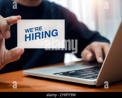 Human resource (HR), people recruitment, recruiting staff, team building concept. Text We're Hiring on white business card, holding by person who work Stock Photo