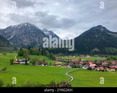 Health resort town in the Oberallgau district, houses in lush green valley with snow on mountains in background Stock Photo