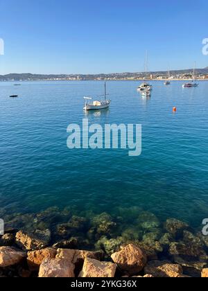 view across bay from breakwater to boats at anchor, man fishing, and Mediterranean coastline Stock Photo