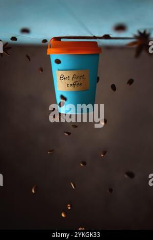 conceptual creative photography of coffee in a takeaway blue cup, with text But first coffee. inverted composition, falling coffee beans Stock Photo