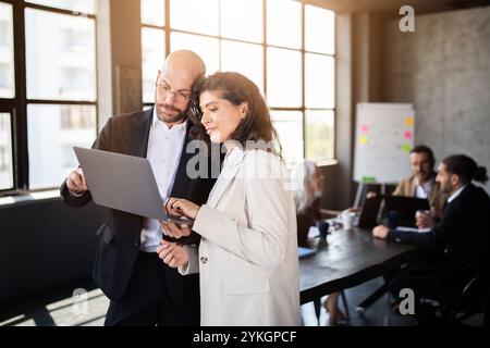 Two professionals collaborating on a laptop in a modern office during a meeting Stock Photo