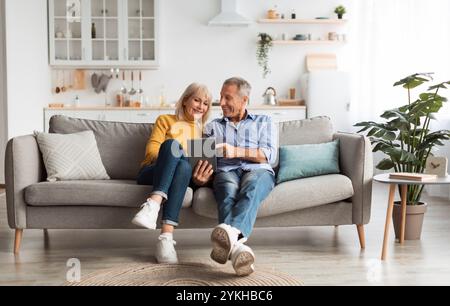 Cheerful Mature Spouses Using Digital Tablet At Home Stock Photo