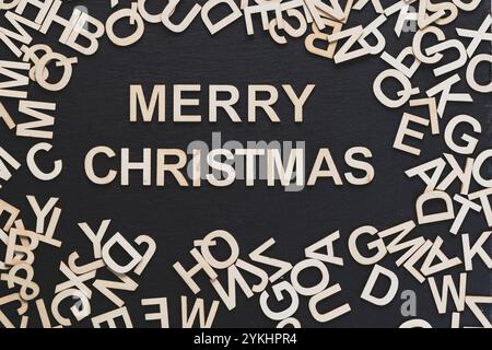 You can see in the image many wooden letters scattered on a blackboard background and a Merry Christmas phrase in the center Stock Photo