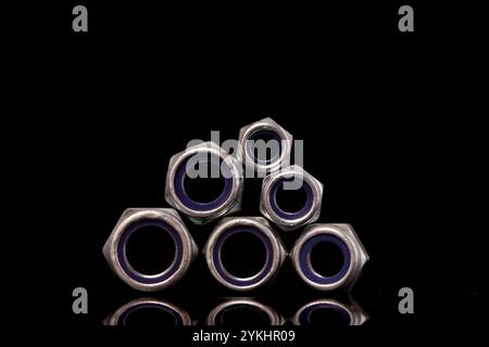 Steel nuts of different sizes on black background with reflecting dark surface. Close up macro shot with copy space. Stock Photo