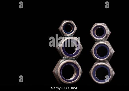 Steel nuts of different sizes on black background with reflecting dark surface. Close up macro shot with copy space. Stock Photo