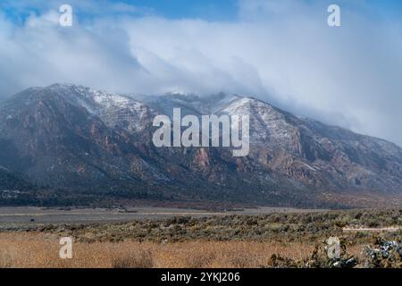 Scenic view of a rugged mountain range with a light dusting of snow under a dramatic, cloudy sky overlooking a dry high desert basin Stock Photo