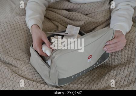 Woman opening gray home first aid kit, pills inside, holding nasal spray, while sitting in bed Stock Photo