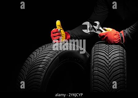 Mechanic hands in gloves Giving Thumbs Up Next to New Car Tires and Wrench, concept for automotive maintenance and quality wheels service in a garage Stock Photo