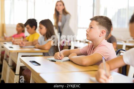 Focused preteen schoolboy writing in workbook at lesson in classroom Stock Photo