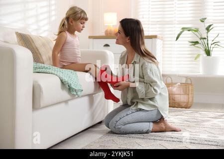 Mother helping her daughter to put tights on at home Stock Photo