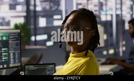 Portrait of smiling computer scientist at work doing software debugging using PC, checking glitches in lines of code. Cheerful IT specialist in office fixing coding issues using computer, camera A Stock Photo