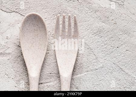 A recycled plastic spoon and fork are seen on a gray cement surface Stock Photo