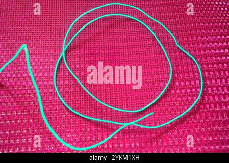 An unusual glowing, electroluminescent green el wire is located on a bright pink background with a hologram reflective effect, small particles. Stock Photo
