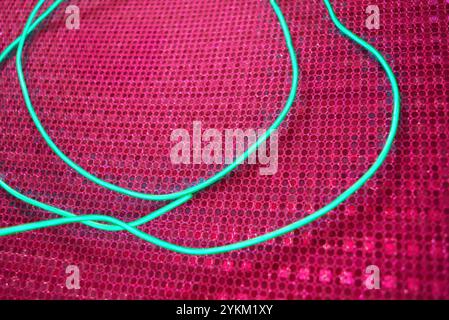 An unusual glowing, electroluminescent green el wire is located on a bright pink background with a hologram reflective effect, small particles. Stock Photo