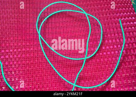 An unusual glowing, electroluminescent green el wire is located on a bright pink background with a hologram reflective effect, small particles. Stock Photo