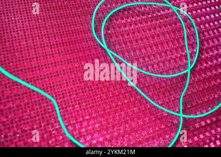 An unusual glowing, electroluminescent green el wire is located on a bright pink background with a hologram reflective effect, small particles. Stock Photo
