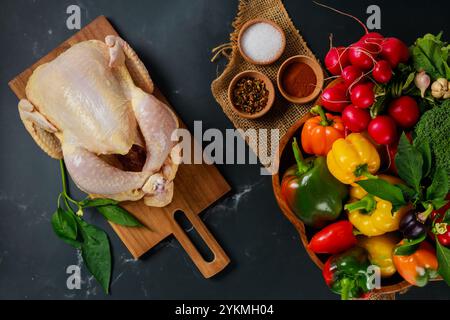 Fresh chicken and vibrant vegetables arranged on dark countertop for preparation of healthy meal Stock Photo