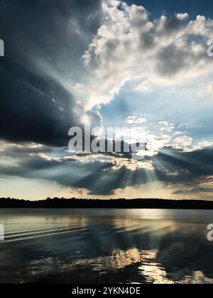 A breathtaking scene of sunrays piercing through dramatic clouds, casting reflections on a serene lake. The landscape evokes tranquility and awe durin Stock Photo
