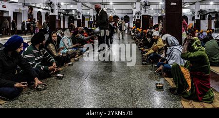 Devotees sit in rows for langar, a free communal meal, inside a sikh temple hall Stock Photo