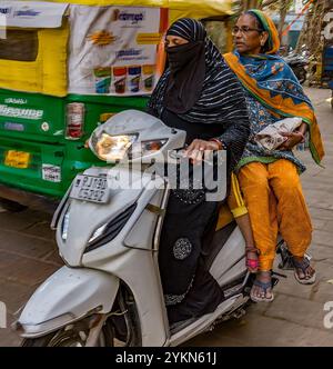 Two indian women, one in traditional attire, ride a scooter in a vibrant street setting Stock Photo