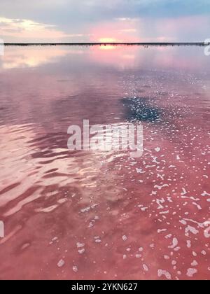 A peaceful scene of a sunset casting warm hues over a calm body of pink water, creating a serene and tranquil ambiance. The water's surface reflects t Stock Photo