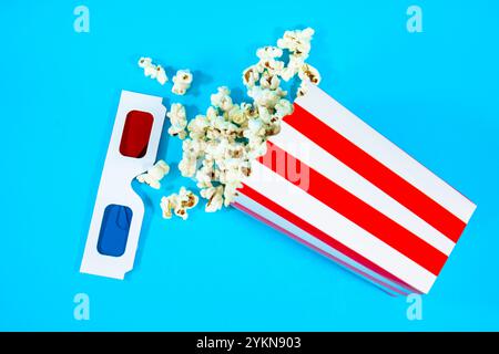 top view of popcorn scattered in a red and white cardboard bucket lying on a blue background, concept of entertainment in the cinema Stock Photo
