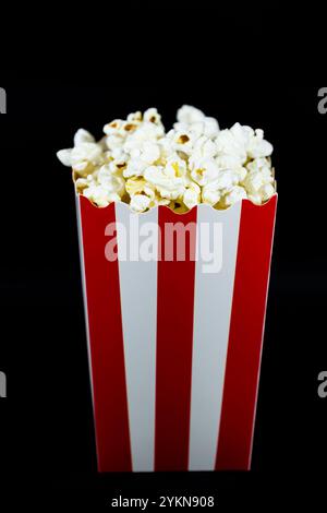 Popcorn in a red cardboard bucket with white on a black background vertical image, concept of entertainment and cinema food Stock Photo