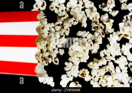 Top view close up of a red and white cardboard bucket lying flat. Scattering popcorn on black background, cinema and popcorn concept Stock Photo