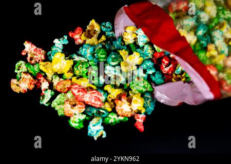 Fallen package with scattered colorful popcorn on a black background, cinema and popcorn concept Stock Photo