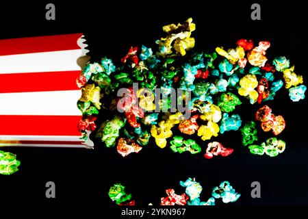 top view of fallen cardboard bucket with scattered colorful popcorn on black background, cinema and popcorn concept Stock Photo