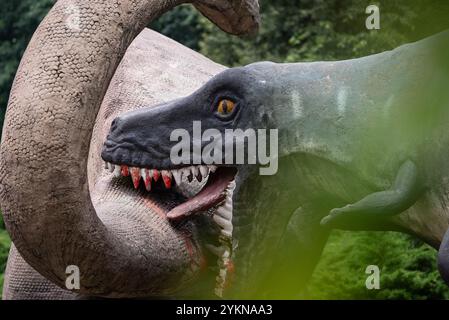 A close up of a dinosaur sculpture in a park, showcasing its detailed design, vibrant colors, and lifelike appearance, blending creativity with paleon Stock Photo