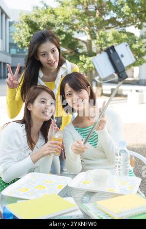 Three female university students taking selfie stick photos in campus cafeteria Stock Photo