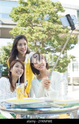 Three female university students taking selfie stick photos in campus cafeteria Stock Photo