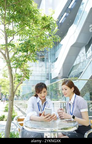 Two office workers drinking iced coffee and looking at their phones Stock Photo