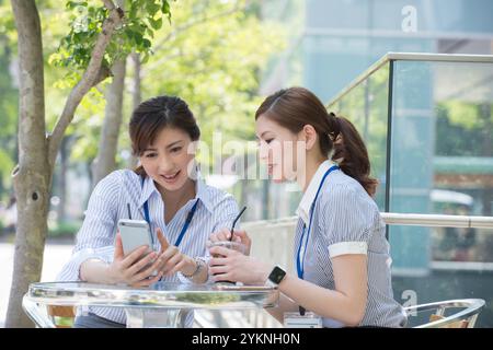Two office workers drinking iced coffee and looking at their phones Stock Photo
