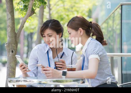 Two office workers drinking iced coffee and looking at their phones Stock Photo