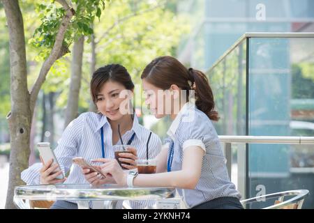 Two office workers drinking iced coffee and looking at their phones Stock Photo