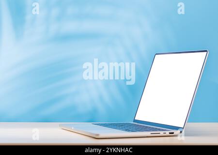 Laptop with a blank white screen placed on a table, sunny wall in the background casting warm light and soft shadows Stock Photo
