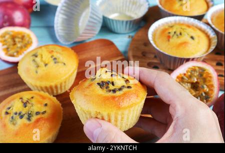 Closeup of Hand Holding a Freshly Baked Homemade Passion Fruit Muffin on Messy Kitchen Table Stock Photo