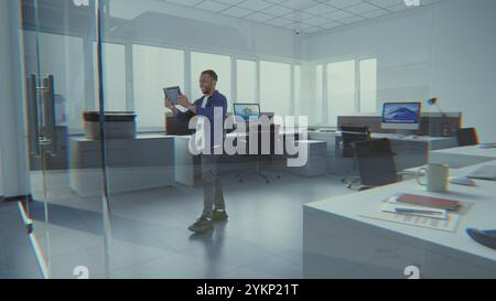 Talented African American designer uses tablet computer and interior design app to decorate office workspace. 3D animation of holographic furniture and digital equipment. Augmented reality technology. Stock Photo