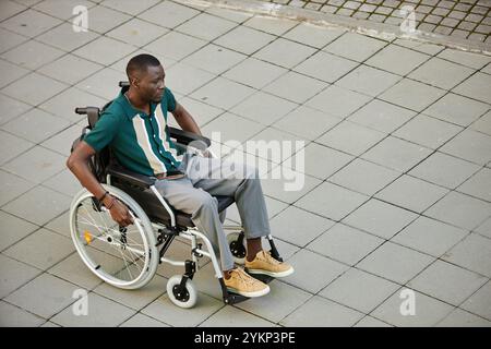 Minimal high angle view at adult African American man using wheelchair while moving in city outdoors on graphic pavement tiles copy space Stock Photo