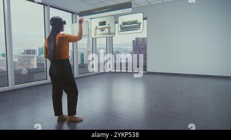 Asian female designer wearing virtual reality headset uses AI augmented reality interior design app to arrange office workspace or stylish apartment with 3D furniture and equipment. 3D visual effects. Stock Photo