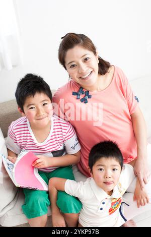 Pregnant mother and siblings with primary school children sitting together on the sofa Stock Photo