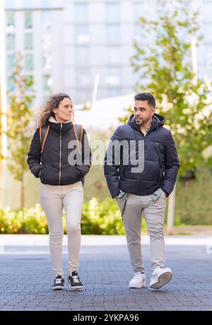 Two university students walking and talking together between classes on a paved walkway on campus Stock Photo