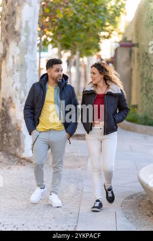 Young multi ethnic couple walking and talking together on a city street enjoying a sunny autumn day Stock Photo