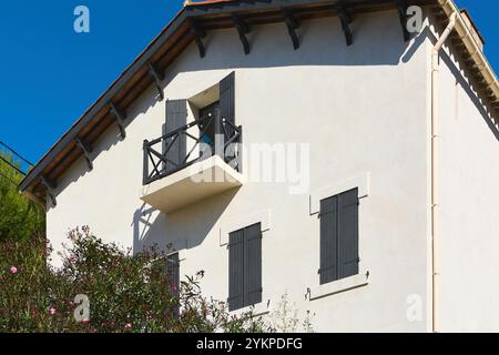 Showcases the upper part of a traditional Mediterranean house with a small balcony featuring black railings and shutters. The light-colored exterior c Stock Photo