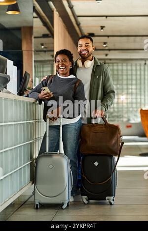 A joyful young couple stands at the hotel lobby, eager to start their vacation journey together. Stock Photo