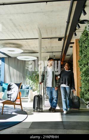 A young couple joyfully navigates a modern hotel lobby, ready for their vacation adventure. Stock Photo